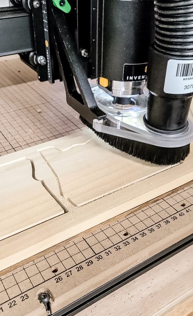 A close up image showing the process of a X-Carve CNC machine cutting an Oregon-shaped cutout into a piece of wood.