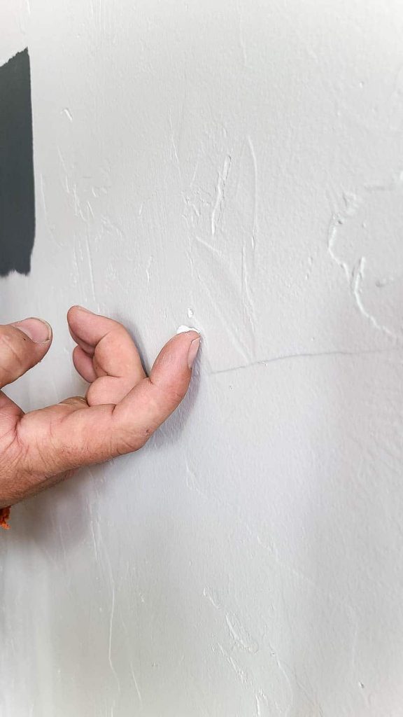 Finger with a pea sized spackling covering the nail hole in the white wall