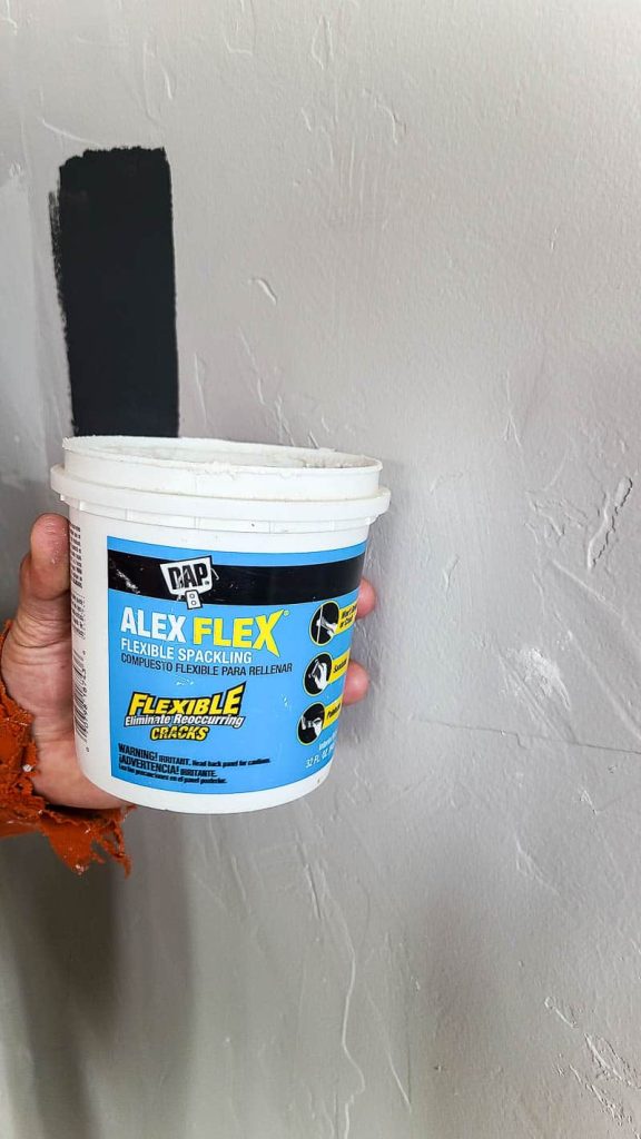 Man holding a small spackling container near the white wall with nail hole