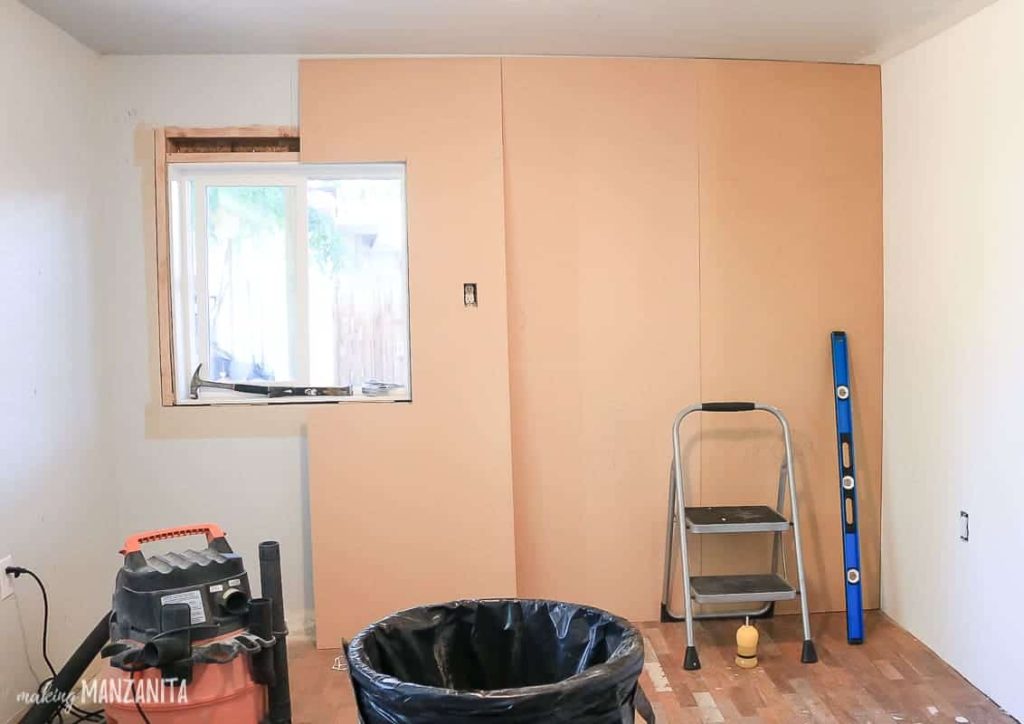 MDF wood covering the wall showing board and batten being installed with ladder, ruler, garbage bin and shopvac