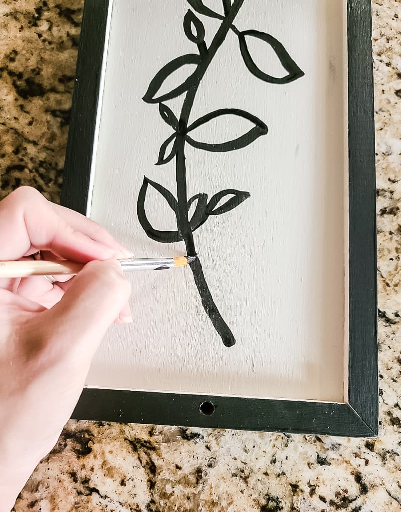 Painting the flower stem outline with black acrylic paint using a paint brush