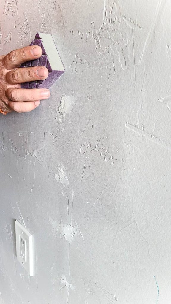 Sanding the spackle on the white wall with sanding block