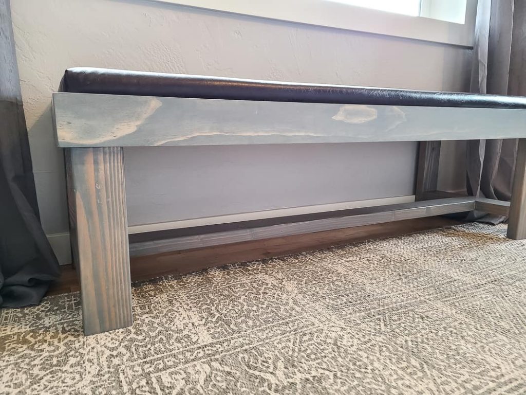 Close up image of bench with DIY bench cushion upholstered with brown leather material sitting in front of window.