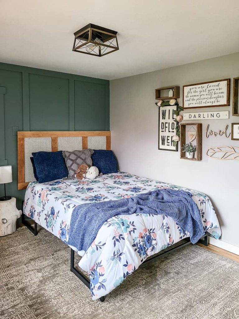View of the little girl's bedroom with bed in floral sheets, blue and grey pillows and diy cane headboard with wall decor