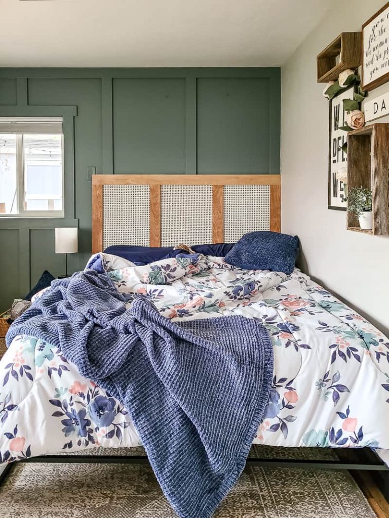 Front view of the bed with blanket, floral sheet, blue pillows and diy cane headboard