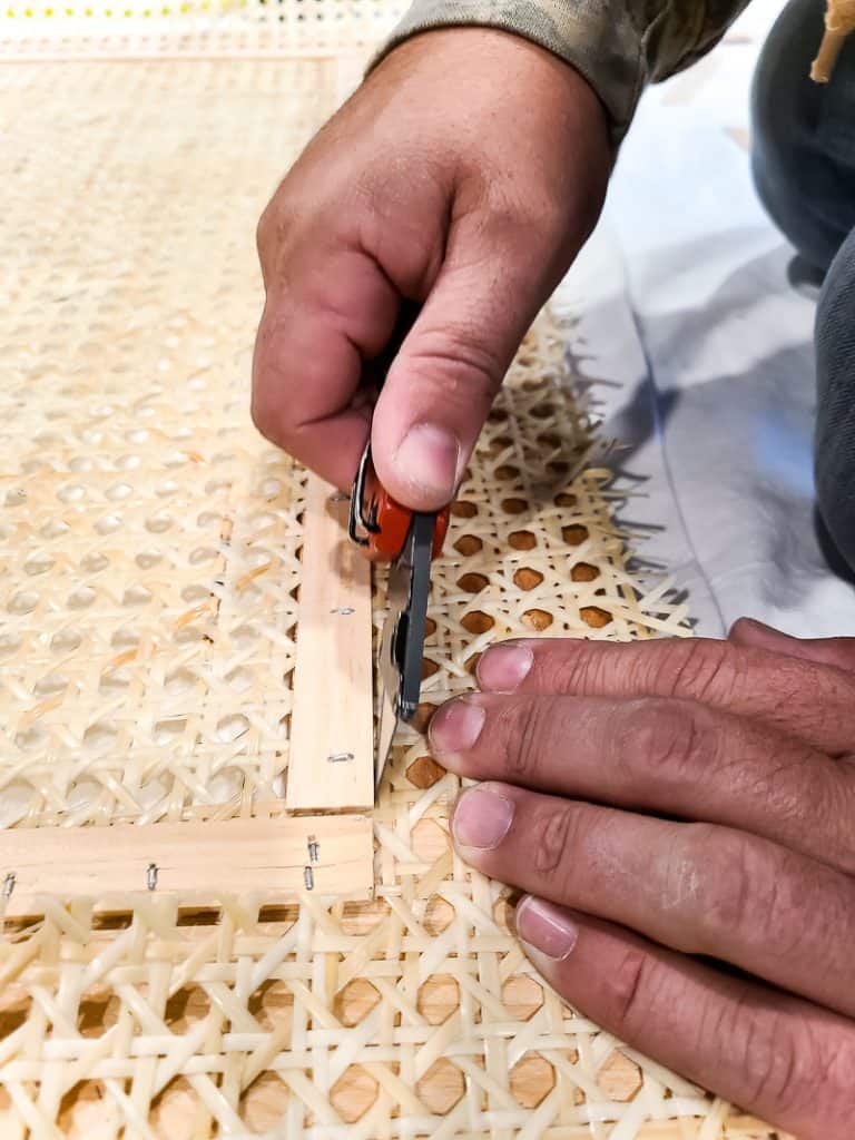 After attaching the cane to the headboard, the man is trimming off any excess cane.