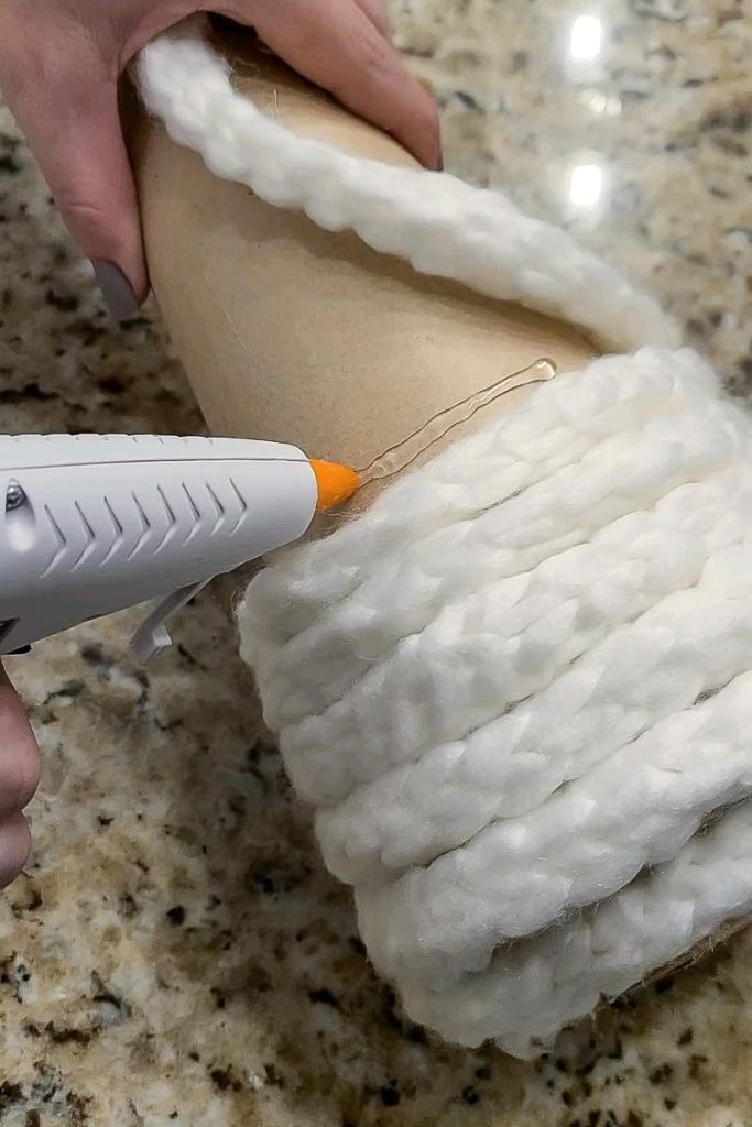 Gluing the white chunky yarn to the cardboard cone using glue gun