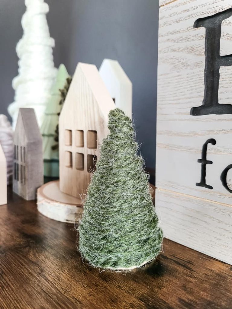 Close up of a mini boho diy yarn Christmas tree and wooden houses at the back