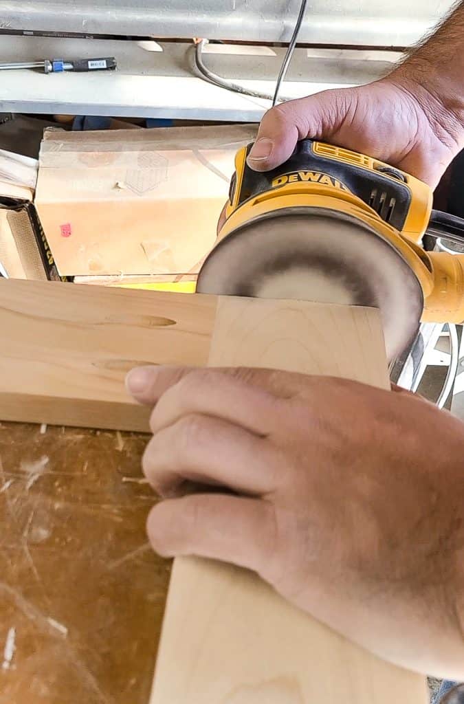 A man is smoothing the surface with an orbital sander as he works on crafting a cane headboard.