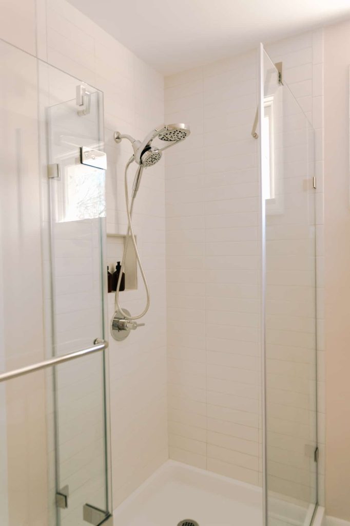 White tiled walk in shower with shower niche positioned behind above the faucet with hand held shower wand extension hanging in front of it.