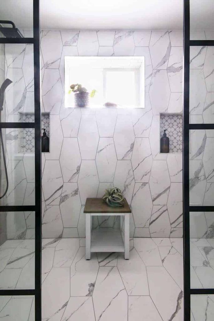 Marble tiled walk in shower with his and hers shower niches with glass amber colored pump bottles.