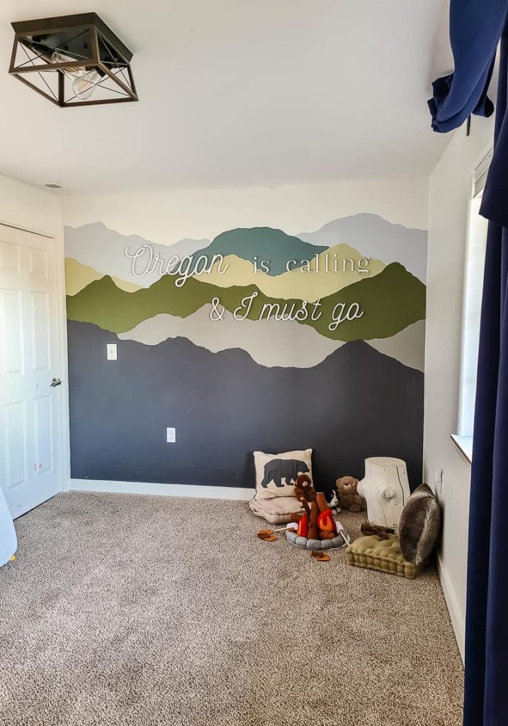 This little boy room with a camping and mountain theme is so fun! I love the John Muir quote on the wall with a mountain mural and play campfire toys. 