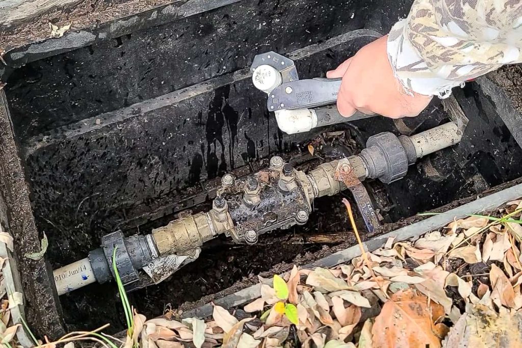 Logan used a wrench to turn water supply line cap to drain excess water before beginning sprinkler blow out. 