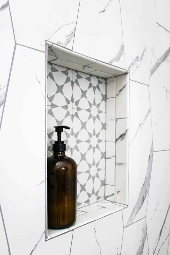 Closeup image of amber glass pump bottle sitting on marble recessed shelf at standing shower niche height.