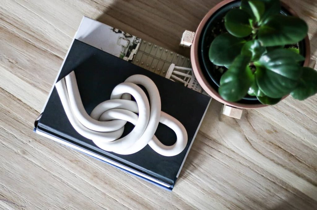 overhead image of clay knot shape on top of books on a light wood coffee table