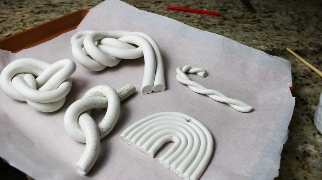 Four knots, a candy cane, and a rainbow made from polymer clay sitting on wax paper ready to go into the oven.