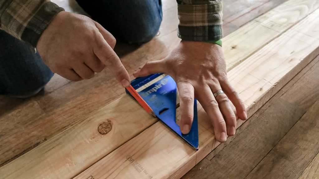 Man drawing a line on two 2x4s using a speed square.