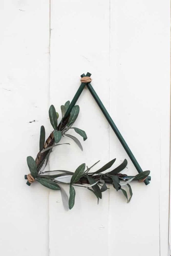 modern boho fall wreath in the shape of a triangle painted green with greenery