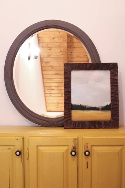 landscape painting in frame next to round mirror