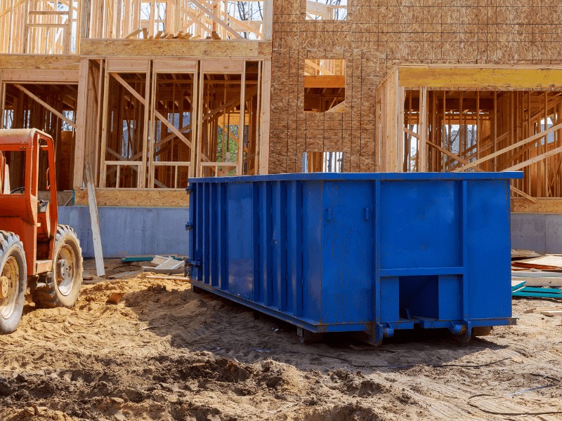 A building site with a blue dumpster sitting in the dirt.  A great place to find free lumber.
