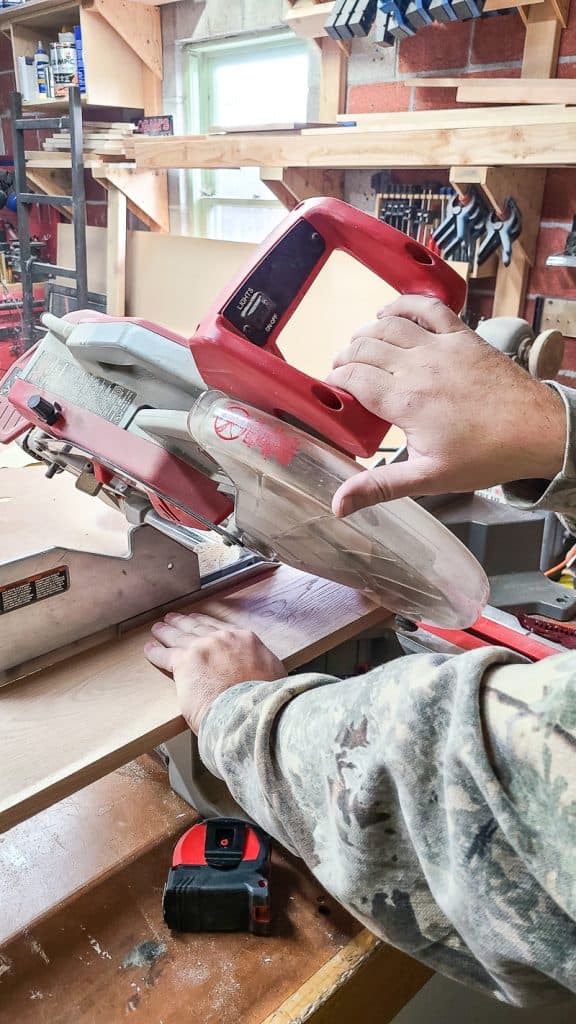 A person expertly cuts wood using a miter saw to craft a Behind-the-Couch Table with Outlet.