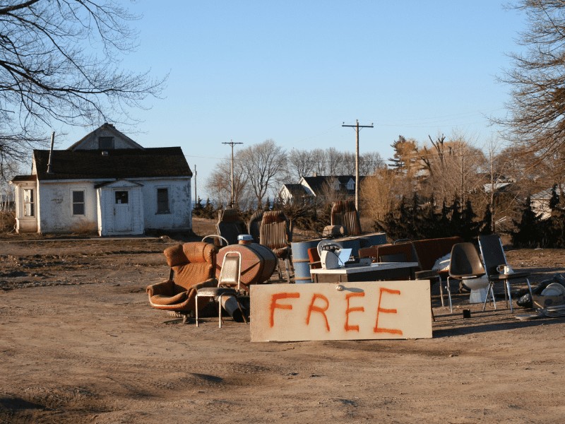Pile of furniture in front of an old white house with FREE painted on a sheet of plywood.