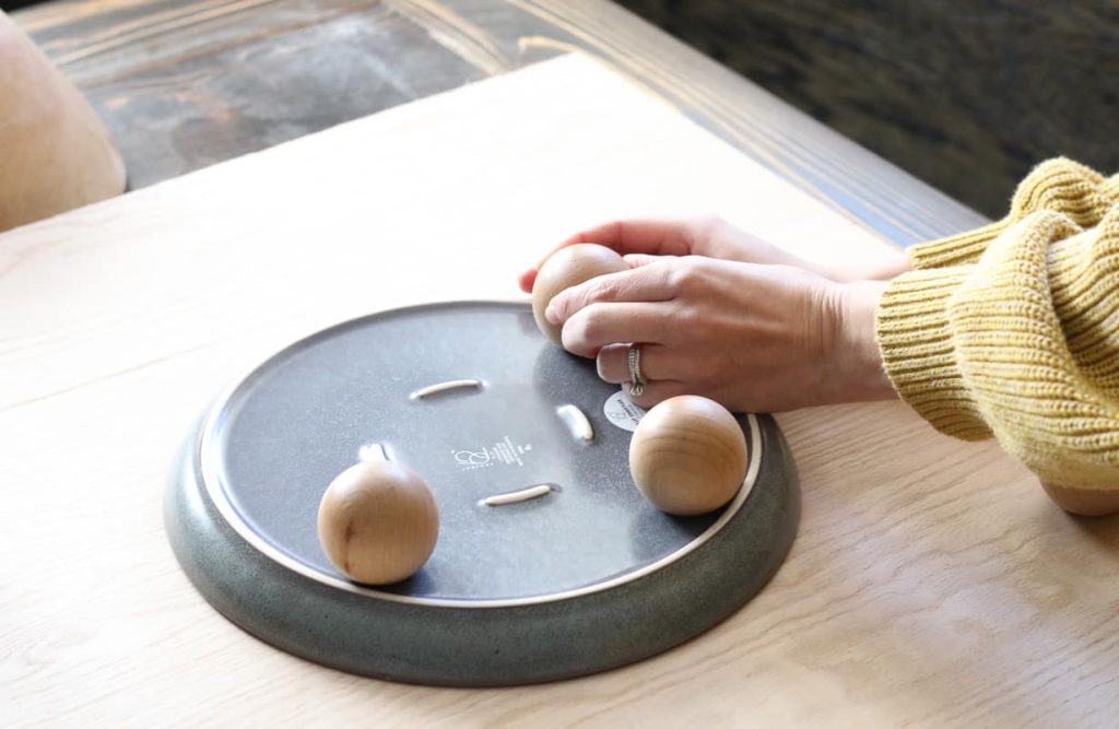 Woman attaching the third wood knob to bottom of ceramic plate to be used as a decorative pedestal tray