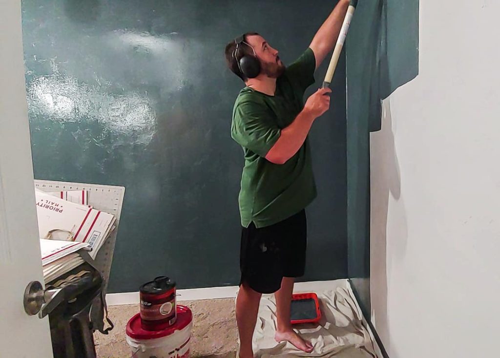 man with ear muffs on painting wall with a paint roller using BEHR Midnight in NY