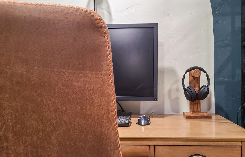 View of DIY headphone stand with headphones sitting on the corner of a desk next to a computer.