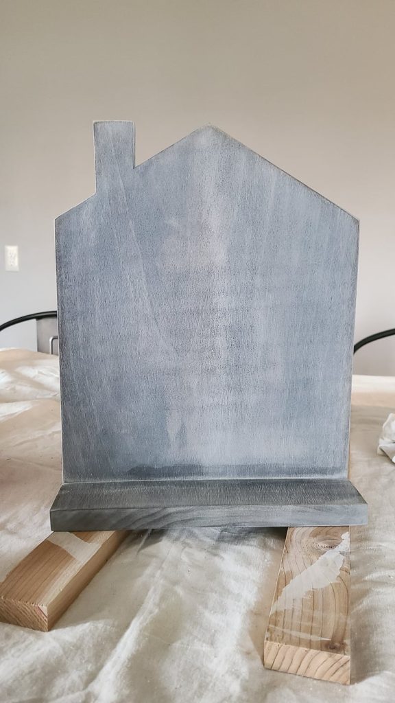 Front of cookbook stand with gray washed wood finish sitting on two pieces of scrap wood on top of paint cloth.