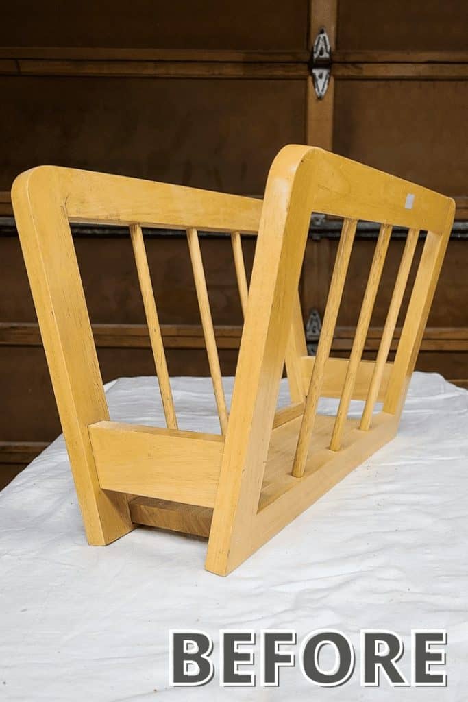 A thrifted wooden magazine holder sits on a drop cloth-covered surface, ready to be painted.