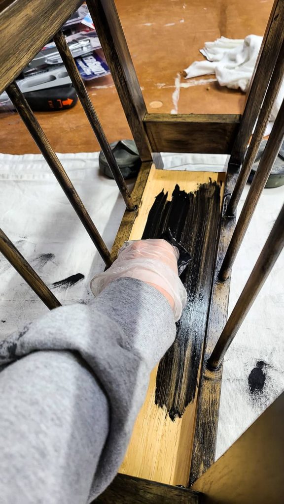 applying black gel stain to magazine rack with rag.