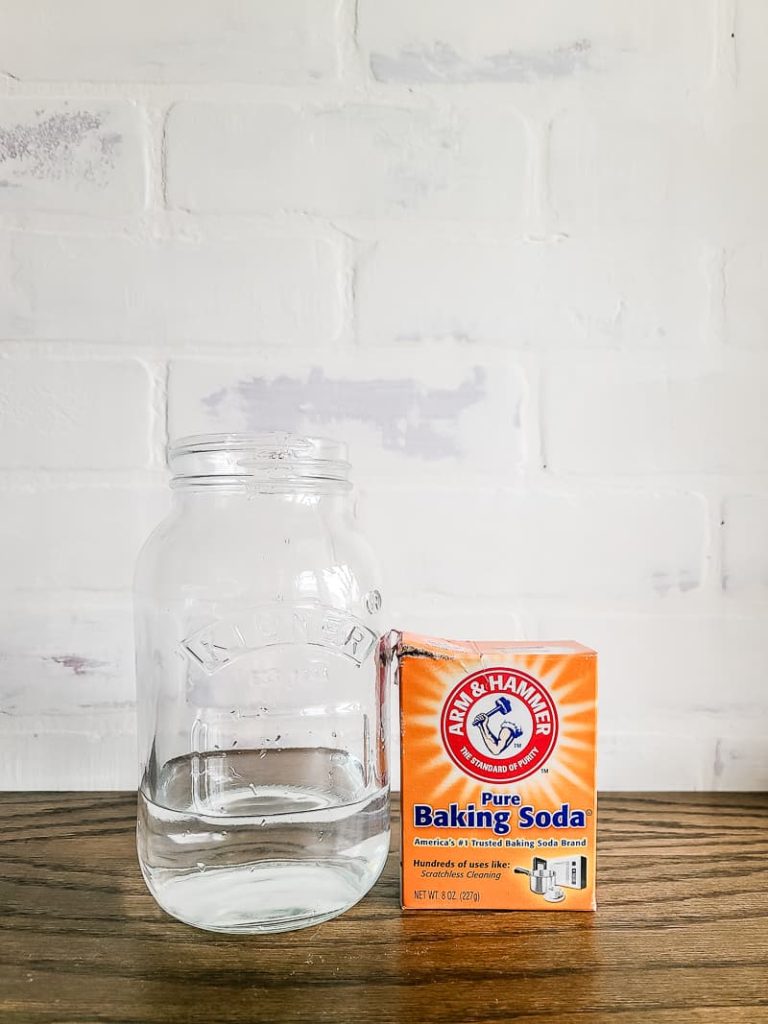 clear jar with water and box of baking soda sitting on wood counter top to use to remove wood stain from hands