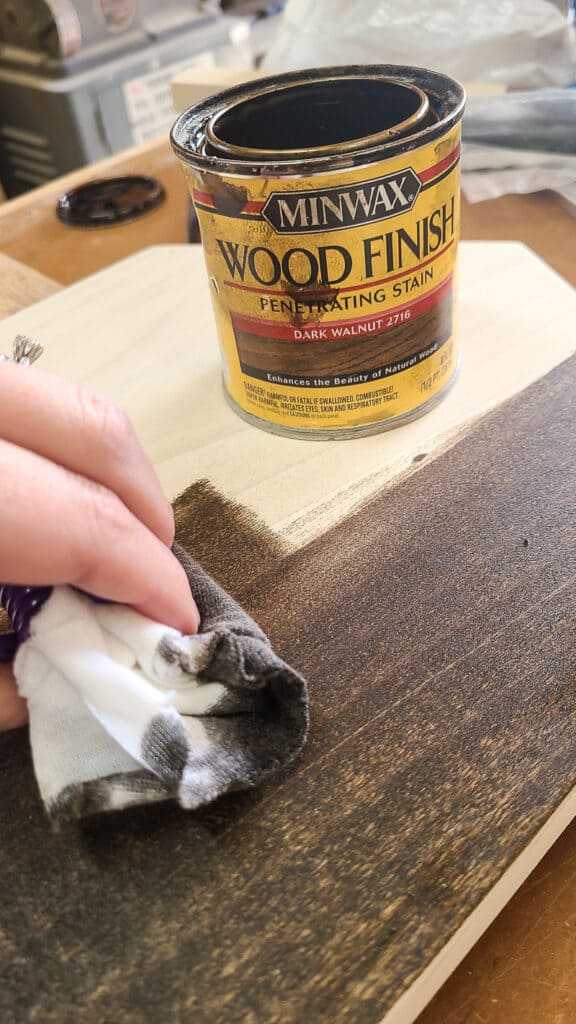 Applying dark walnut stain with a rag to a piece of wood.