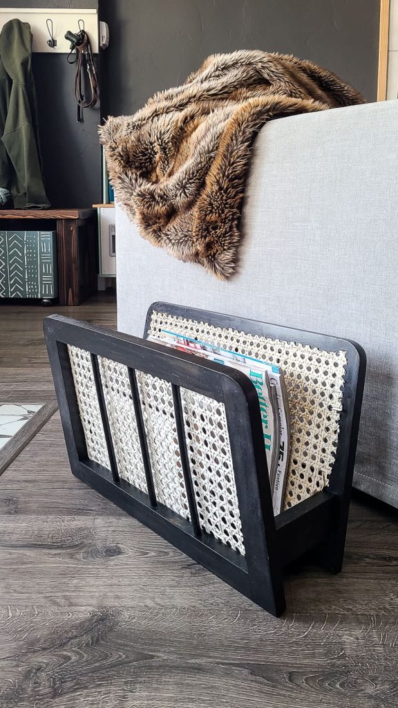 black magazine rack with cane netting next to gray sofa.