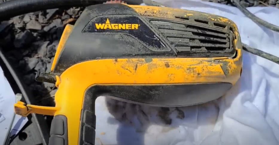 A black and yellow Wagner FLEXiO 3000 Paint Sprayer, scuffed up with paint and markings, rests on a white sheet.