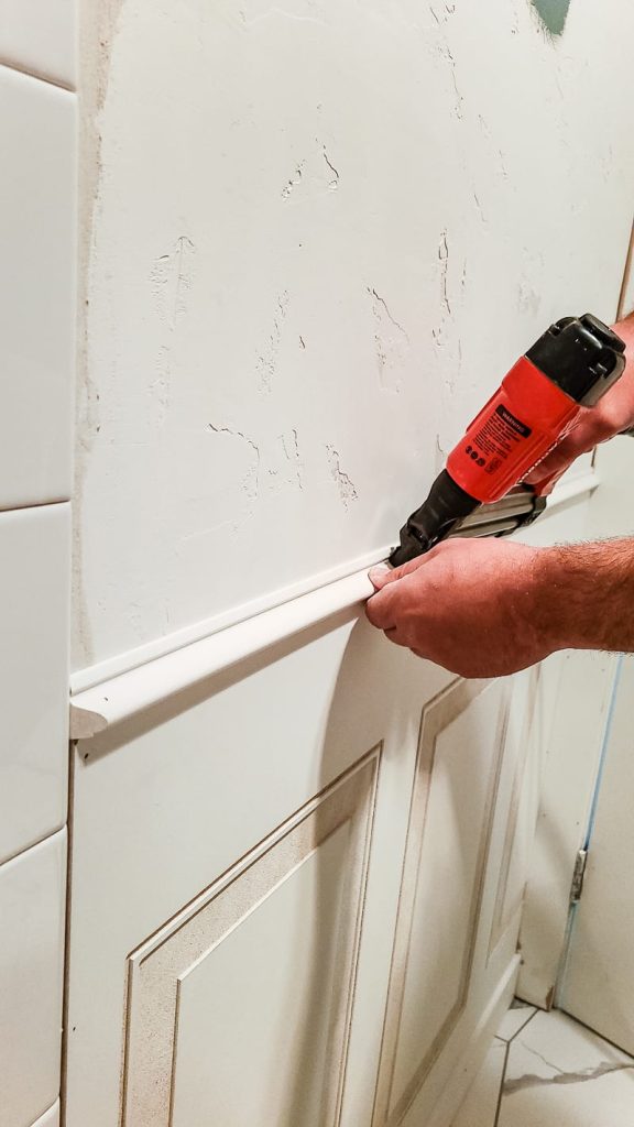 Installing molding above wainscoting panel using a brad nailer and brad nails.