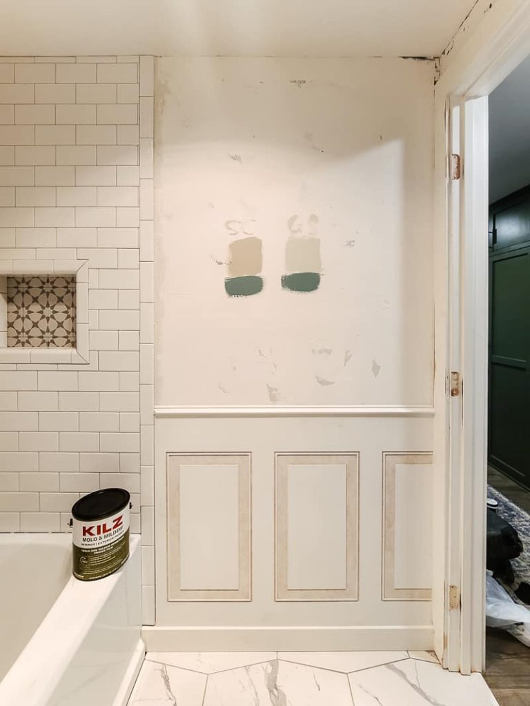 Paint colors tested on the wall above decorative molding with can of KILZ sitting on ledge of bathtub