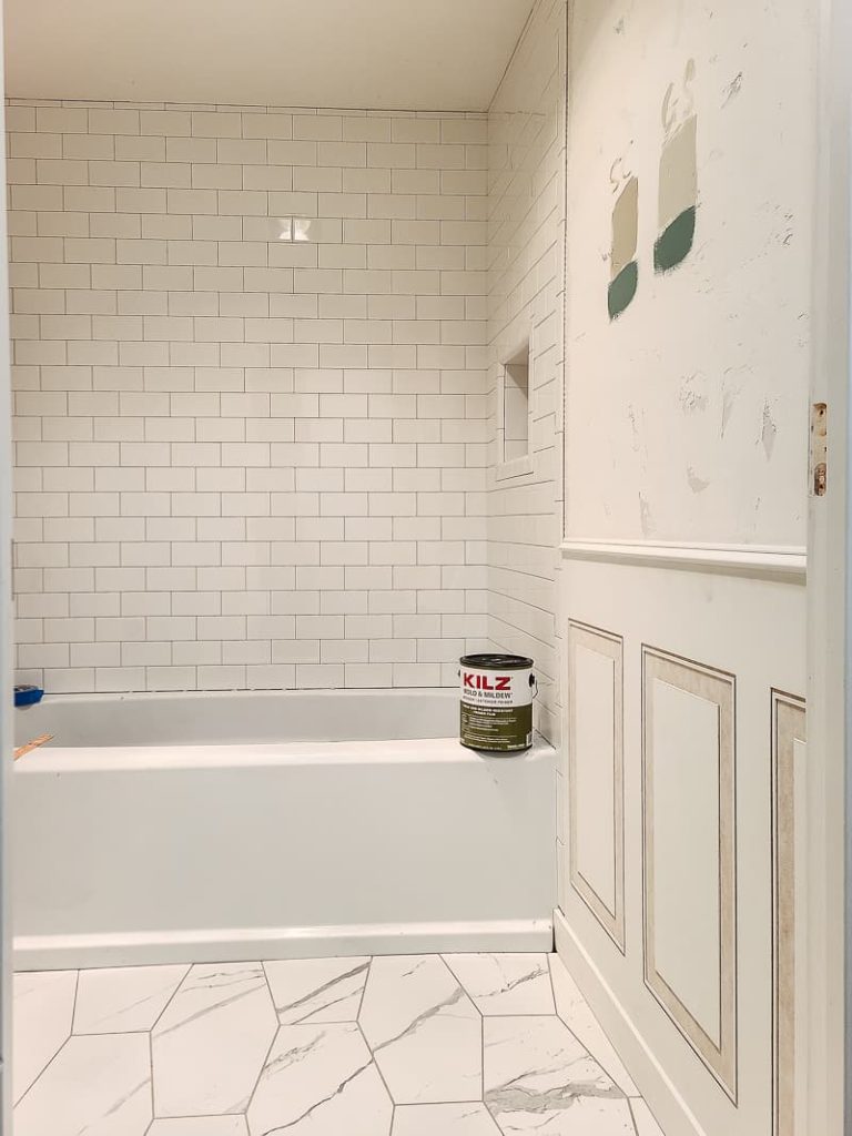 View of bathtub with can of KILZ for primer for bathroom sitting on the rim with paint colors tested on the wall above decorative molding.