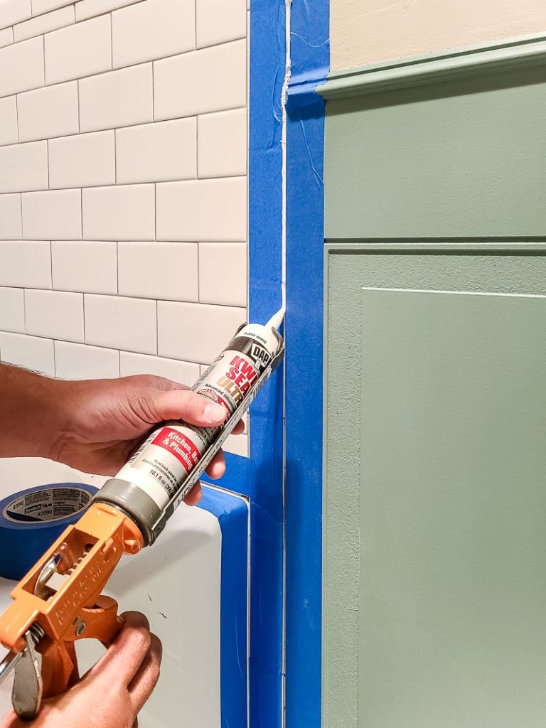 Applying DAP kitchen and bath sealer to edge between wainscoting and bathtub.