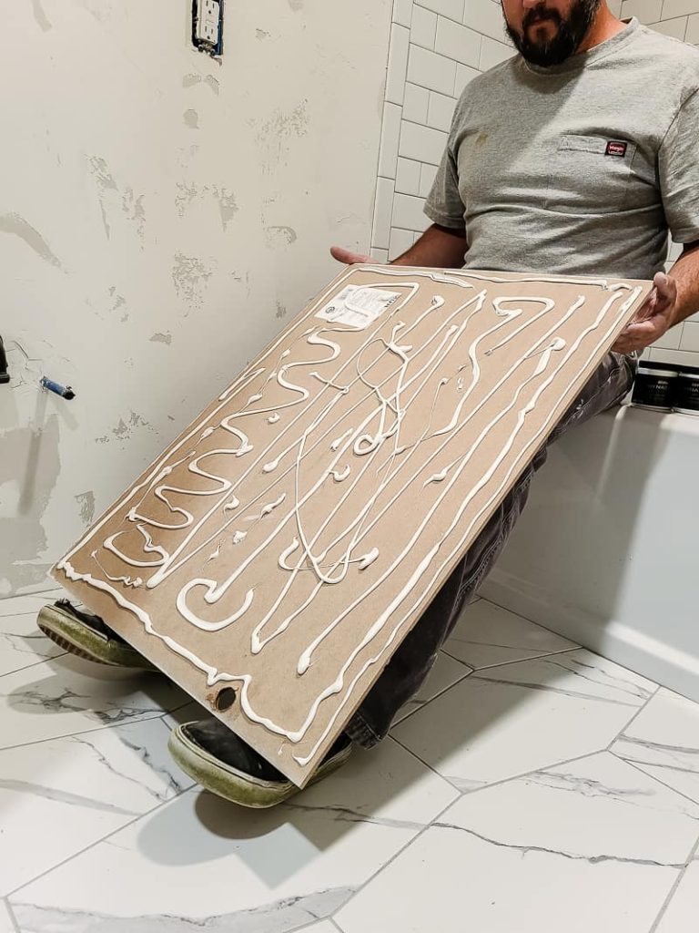 Man holding wainscoting panel on his feet while sitting with glue applied all over the back of the panel.