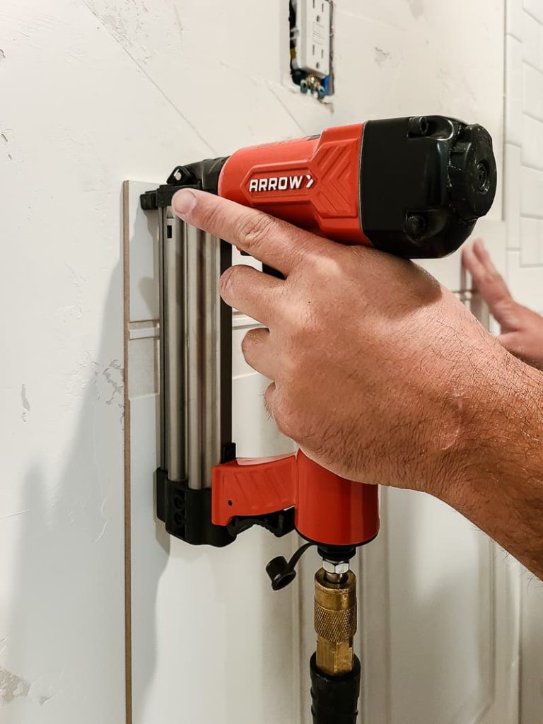 Securing the wainscoting panel using a brad nailer and brad nails.