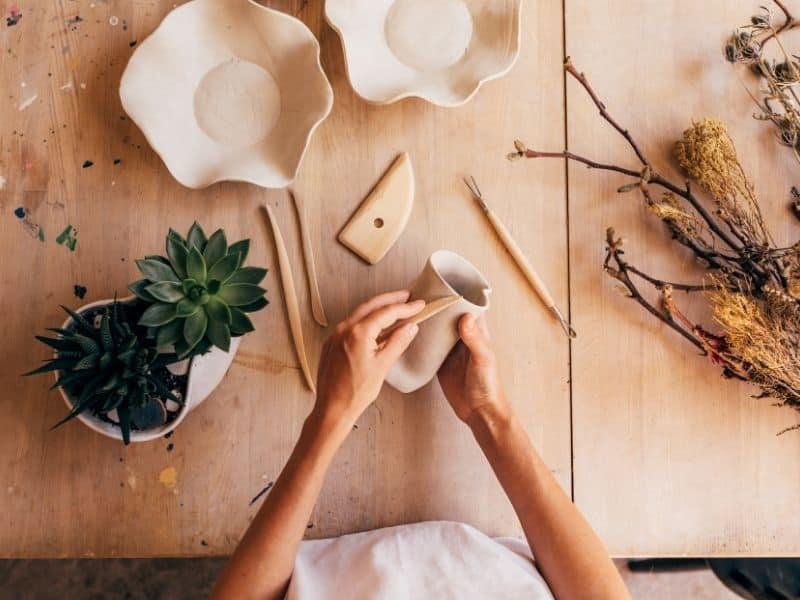 Over head view of a woman sculpting an air dry clay vase using a sculpting tool