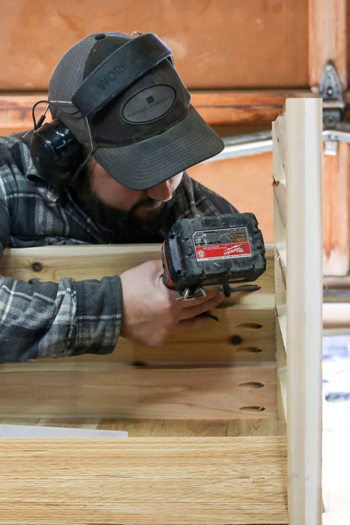 The man is attaching the side planks to construct the Outdoor Toy Deck Box.