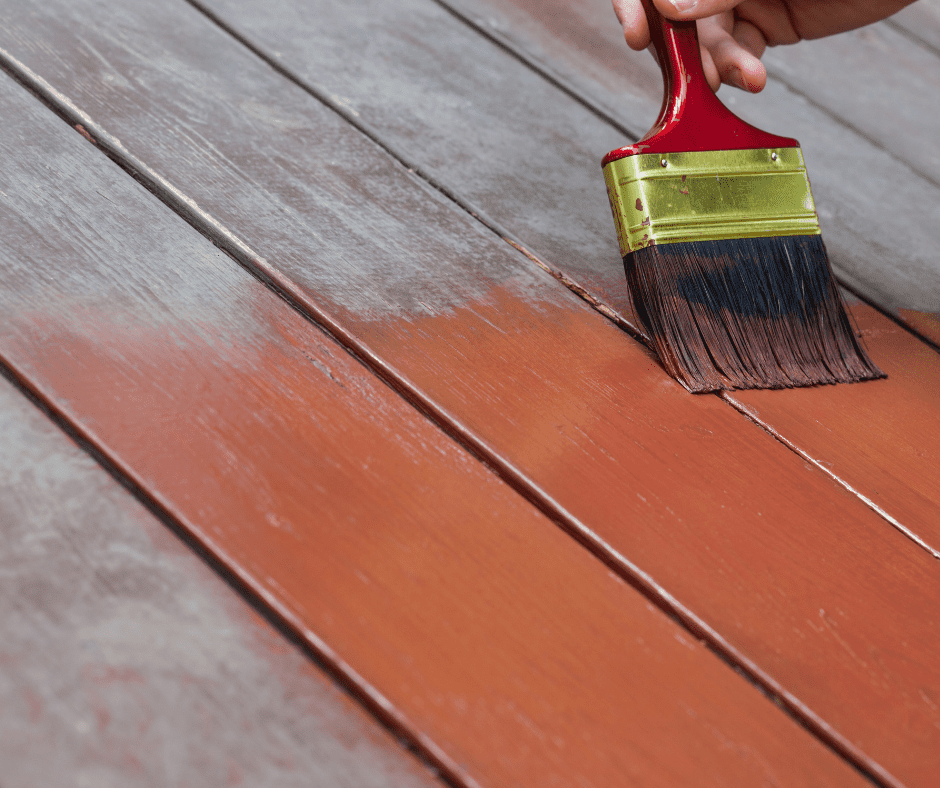 Applying deck stain with a paint brush to change the color of the wood and protect it.