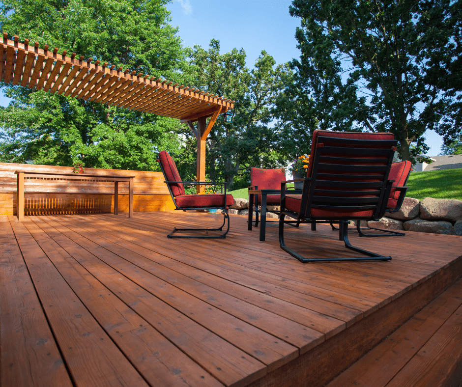 View of deck with pergola, a table and seating area with four chairs with red cushions.