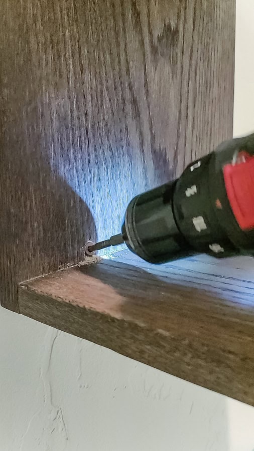 Attaching wooden shelf for towels to the wall with 2" wood screws and drill 