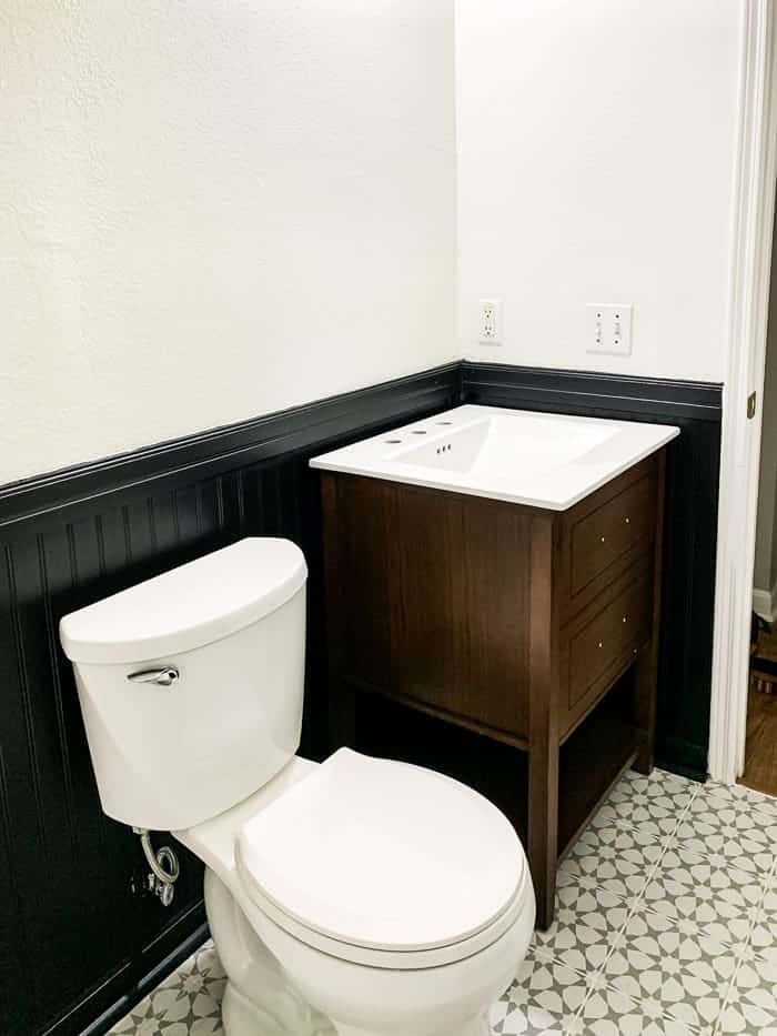 Beadboard feature painted black halfway up the wall behind the toilet and sink in the bathroom.