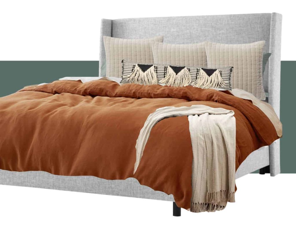 A boho style bedding mood board shows a collage of bedding elements edited together -- a gray padded upholstered headboard, rust colored comforter and cream throw blanket at the end of the bed, and two rows of three pillows.