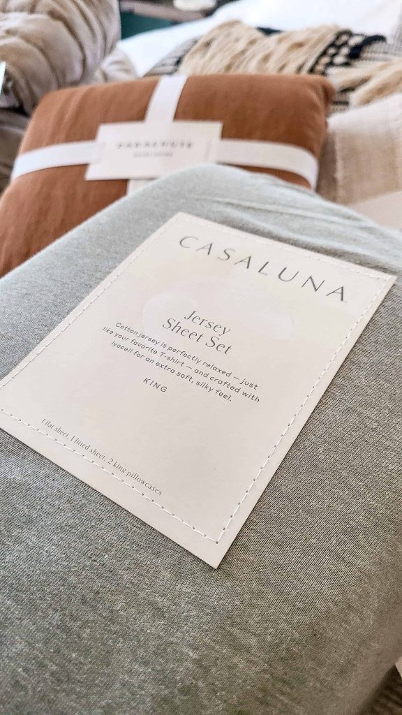 A close up image of a package of Casaluna jersey bed sheets. The sheets come packaged in a gray jersey material sack with a cream-colored label on the front.